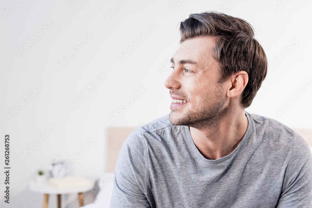 Obraz premium handsome man in grey t-shirt smiling and looking away at home