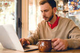 concentrated blogger looking at laptop while holding cup of coffee