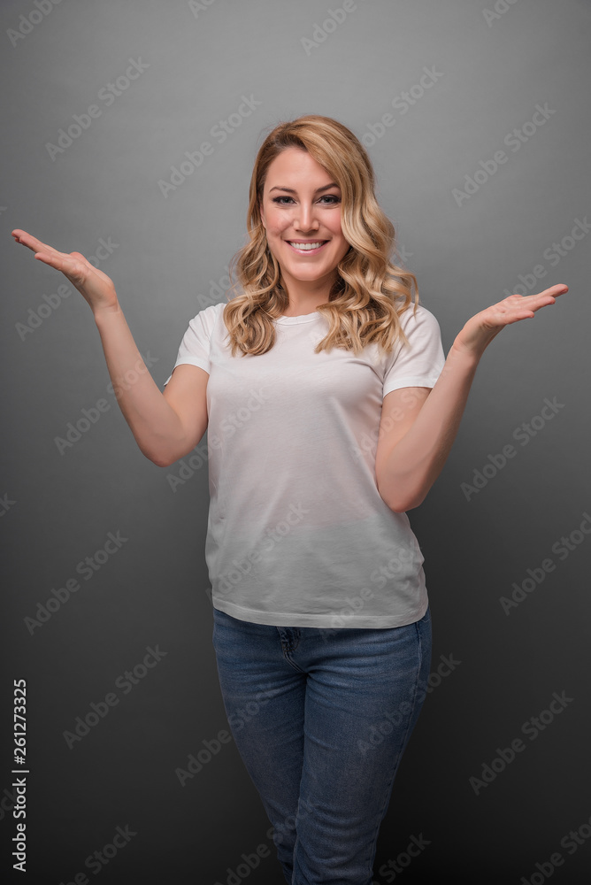 Beautiful blonde is smiling and shows fingers in different directions. Studio photo of a young attractive woman on a gray background. Beautiful blonde is smiling and shows fingers in different directions. Studio photo of a young attractive woman on a gray background.