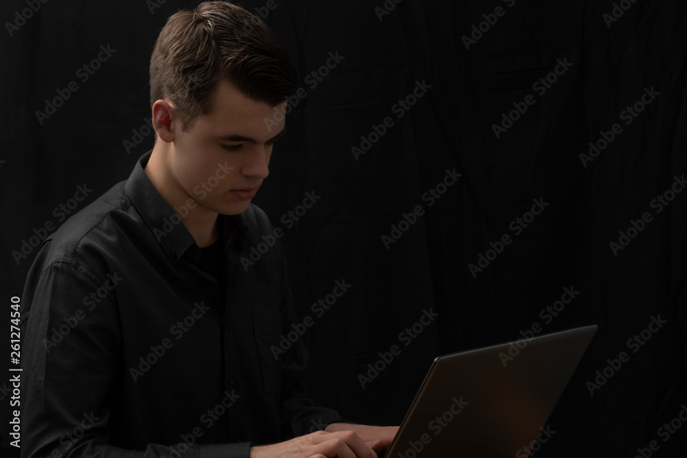 Handsome young businessman seen from the right typing on his laptop. Black background. Handsome young businessman seen from the right typing on his laptop. Black background.