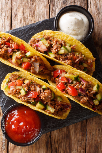 Authentic tacos with minced beef, cheese and vegetables are served with sauces close-up. Vertical top view