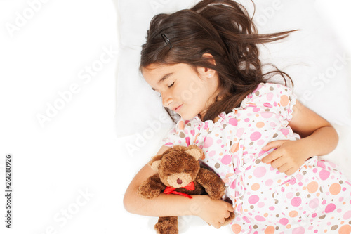 Cute little girl sleeping with teddy bear in bed. Isolated on white background