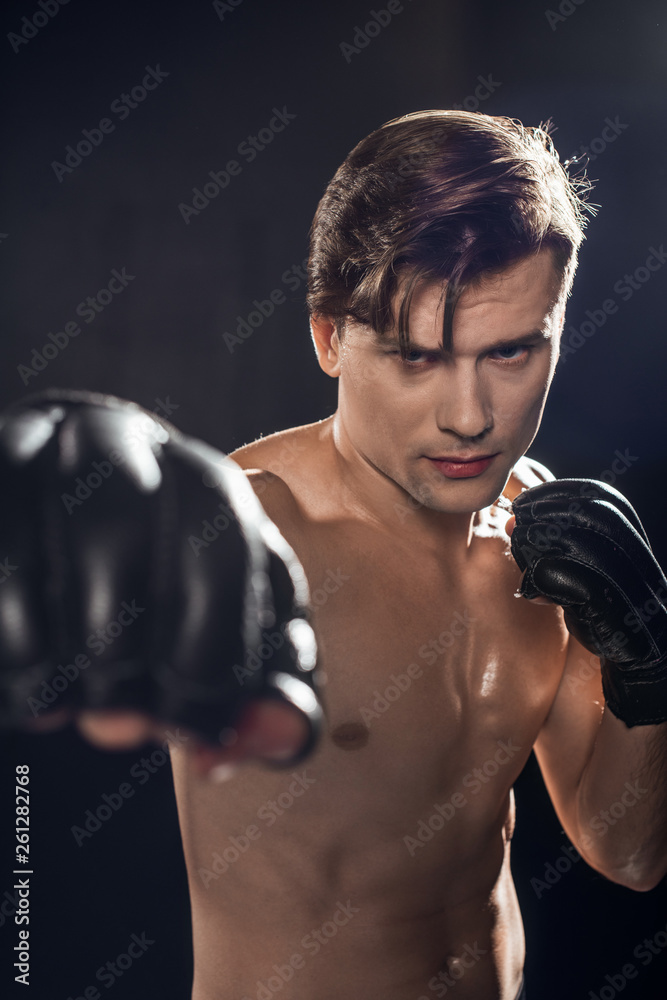 Selective focus of concentrated boxer in boxing gloves training and looking at camera Selective focus of concentrated boxer in boxing gloves training and looking at camera