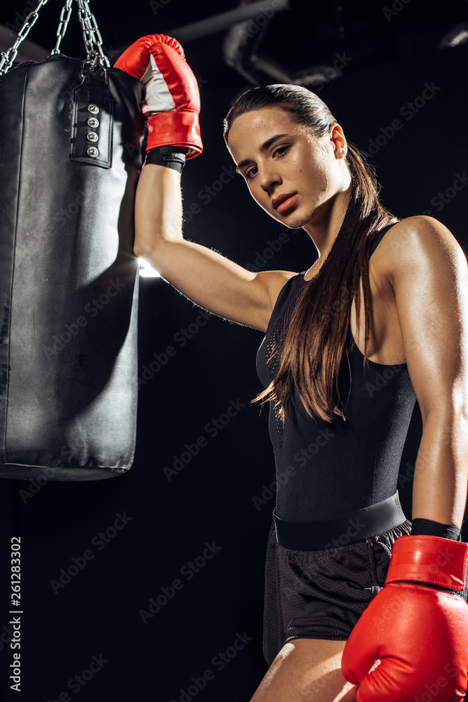 Female boxer in red boxing gloves standing near punching bag