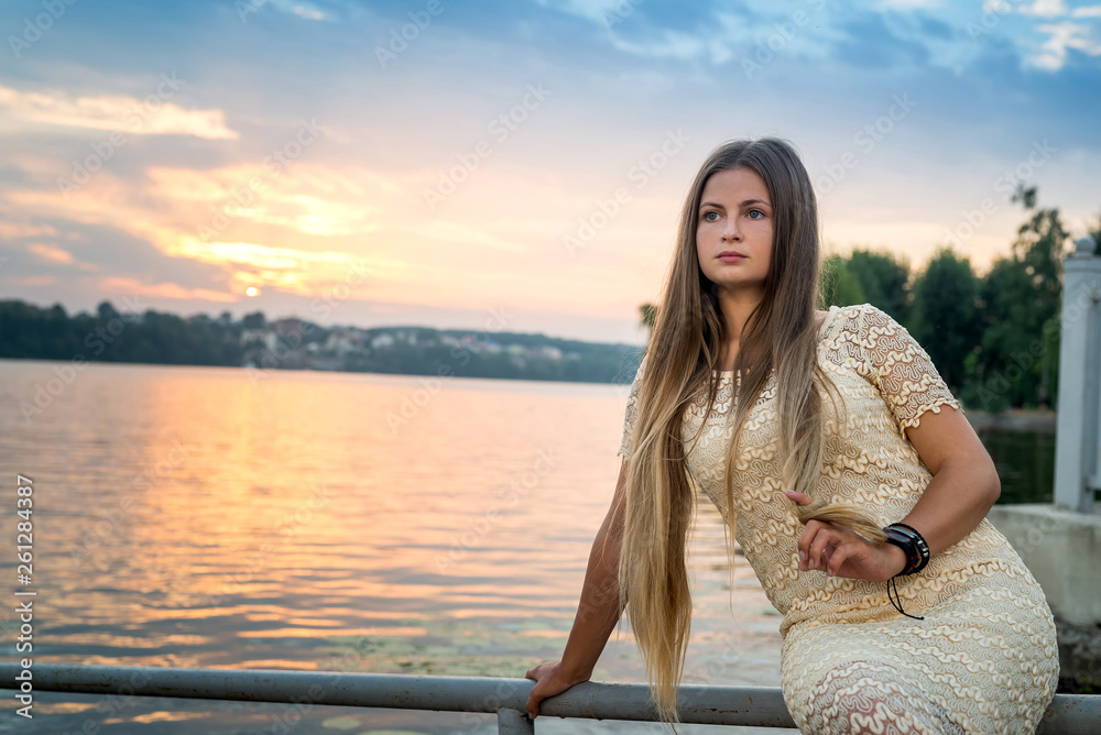Young attractive woman in fashion dress posing against sunset