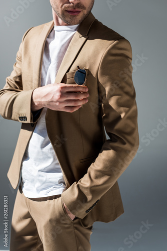 cropped view of man in beige suite with hand in pocket on grey