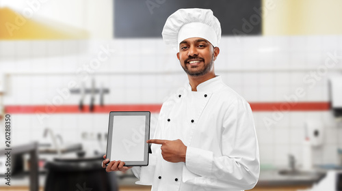 cooking, technology and people concept - happy male indian chef in toque with tablet computer over restaurant kitchen background
