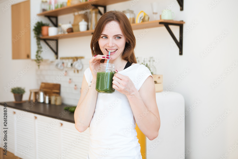 Smiling young woman drinking green smoothie juice in kitchen. Healthy Lifestyle. Smiling young woman drinking green smoothie juice in kitchen. Healthy Lifestyle.