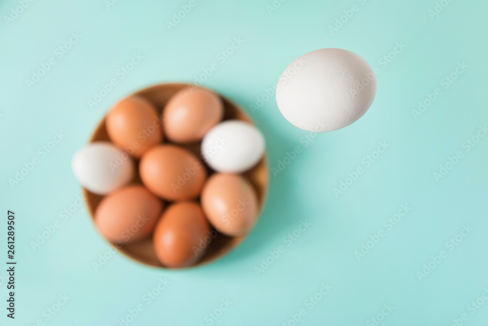 White egg falls in a wooden plate with eggs on a blue table. Happy Easter. Selective focus. Top view