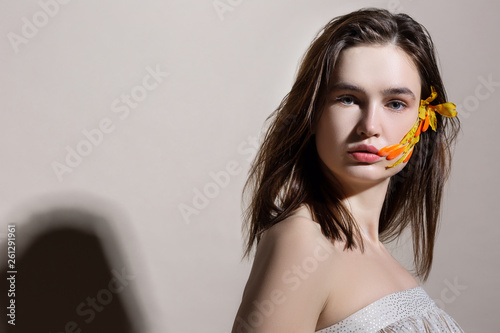 Model with thick eyebrows posing with orange flower in hair