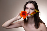 Blue-eyed model with light pink lips posing with orange flower