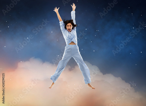 fun, people and bedtime concept - happy young woman full of energy in blue pajama jumping over starry night sky background