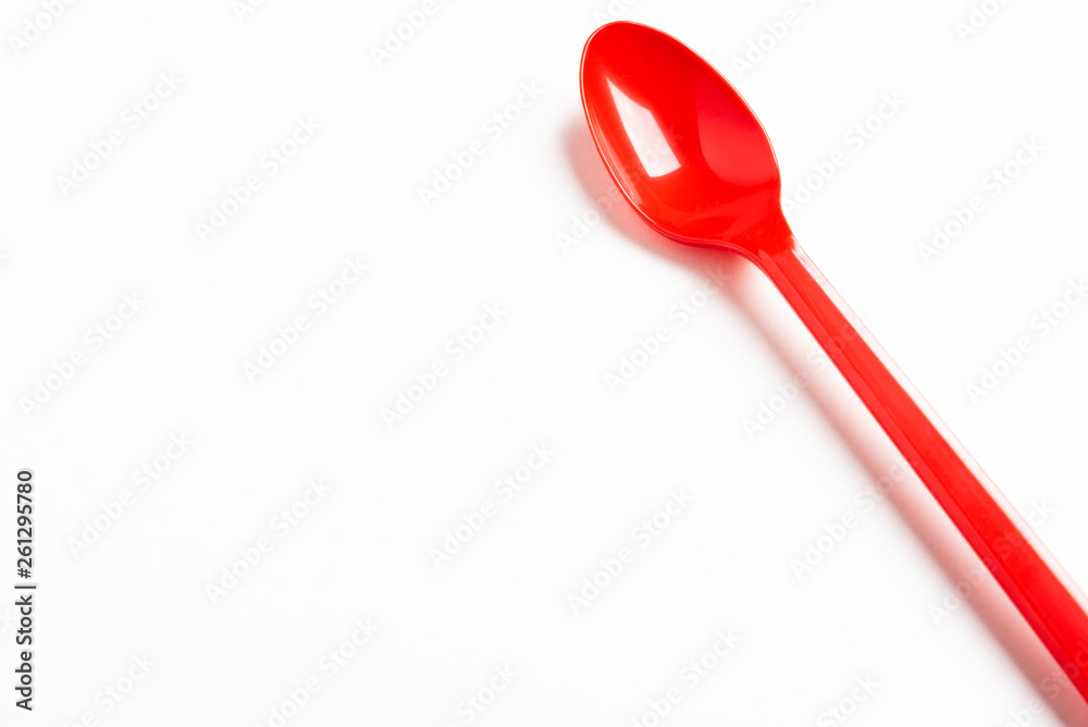 A single long and unused shiny red plastic spoon deliberately and artistically set on a plain white background. A single long and unused shiny red plastic spoon deliberately and artistically set on a plain white background.