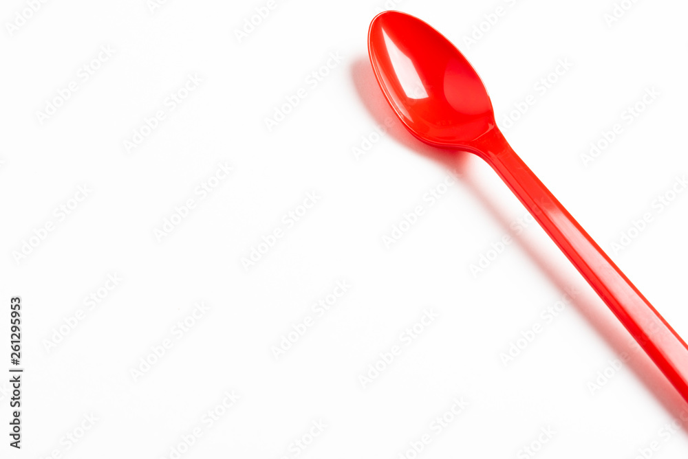 A single long and unused shiny red plastic spoon deliberately and artistically set on a plain white background.