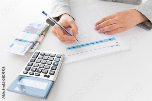 business and finances concept - close up of businesswoman with tax form, calculator and money on office table