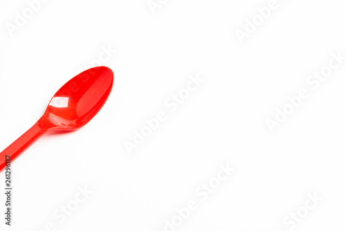 A single long and unused shiny red plastic spoon deliberately and artistically set on a plain white background.