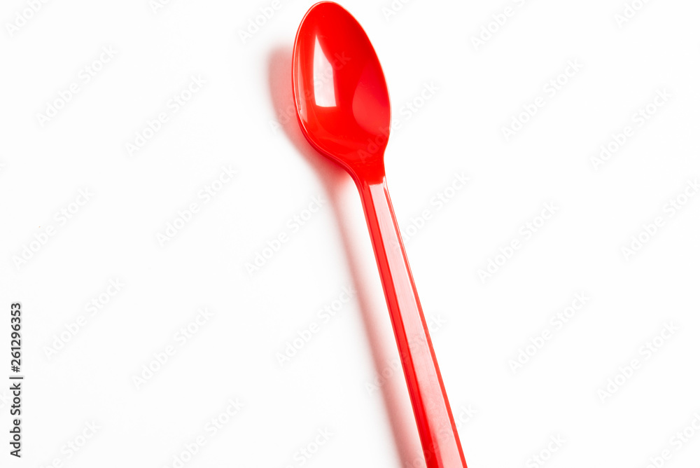 A single long and unused shiny red plastic spoon deliberately and artistically set on a plain white background.