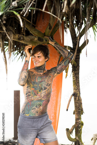 Photography Attractive male surfer in tattoos on the ocean with an orange bright longboard surfboard
