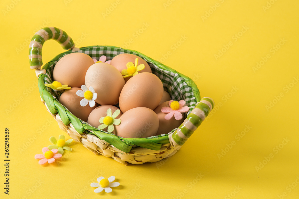 Close up. Easter still life. Rustic eggs in a wicker basket lined with checkered fabric. Yellow background. Copy space.