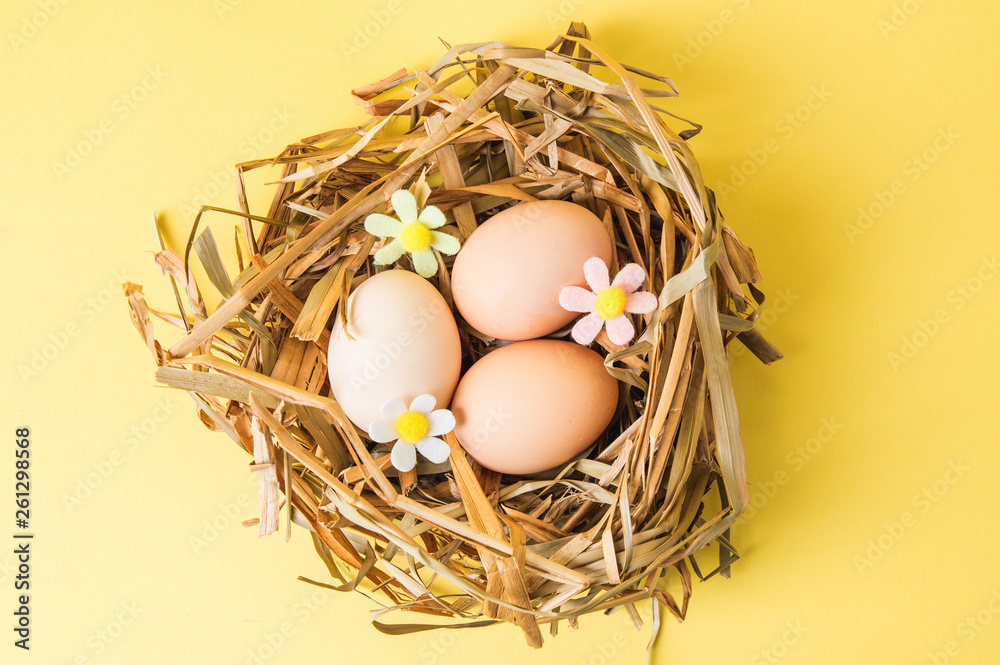 Top view. Easter. Rustic eggs in a nest of straw. The decor of the felt flowers of pastel colors. Yellow background. Copy space. Top view. Easter. Rustic eggs in a nest of straw. The decor of the felt flowers of pastel colors. Yellow background. Copy space.