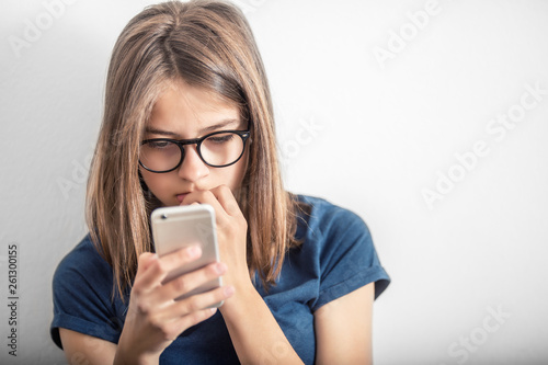 Cute young girl in blue shirt reads message or video to mobile phone