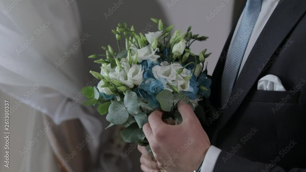 Groom with wedding bouquet in his hands at home. White shirt, blue tie, jacket Groom with wedding bouquet in his hands at home. White shirt, blue tie, jacket
