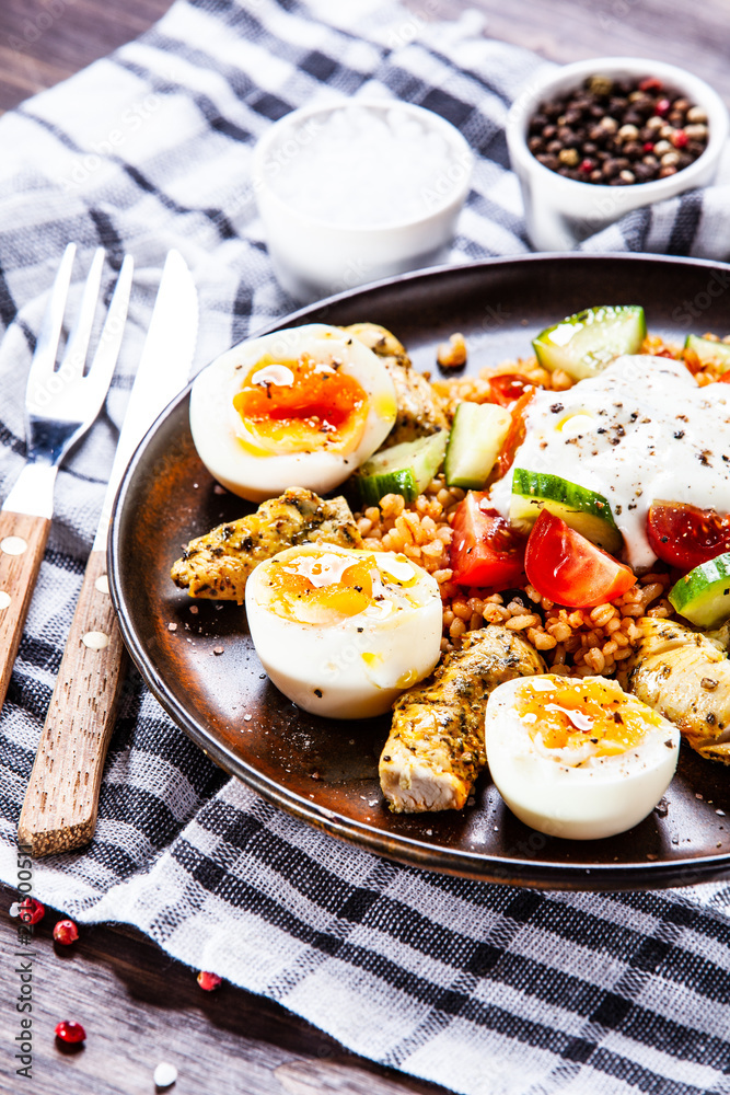 Grilled chicken meat with groats and boiled egg on wooden table