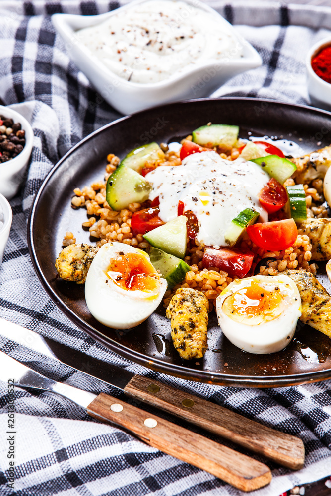 Grilled chicken meat with groats and boiled egg on wooden table Grilled chicken meat with groats and boiled egg on wooden table