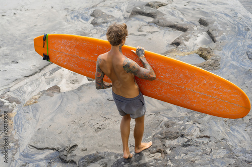 Photography Attractive male surfer in tattoos on the ocean with an orange bright longboard surfboard