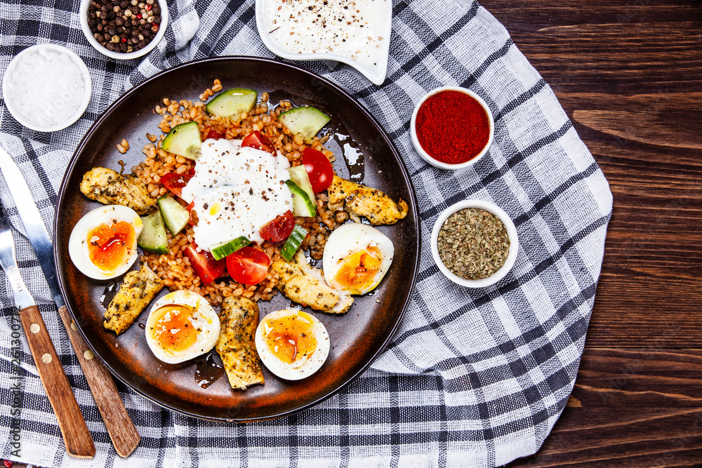 Grilled chicken meat with groats and boiled egg on wooden table Grilled chicken meat with groats and boiled egg on wooden table
