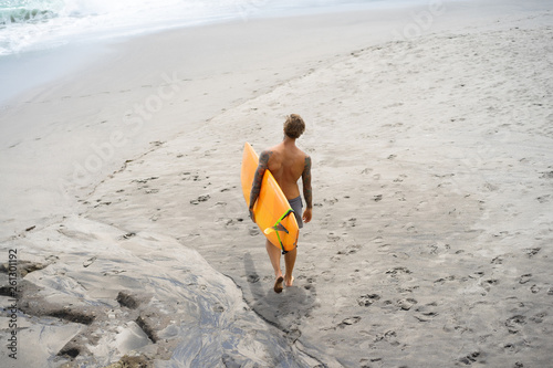 Canvas Print Attractive male surfer in tattoos on the ocean with an orange bright longboard surfboard