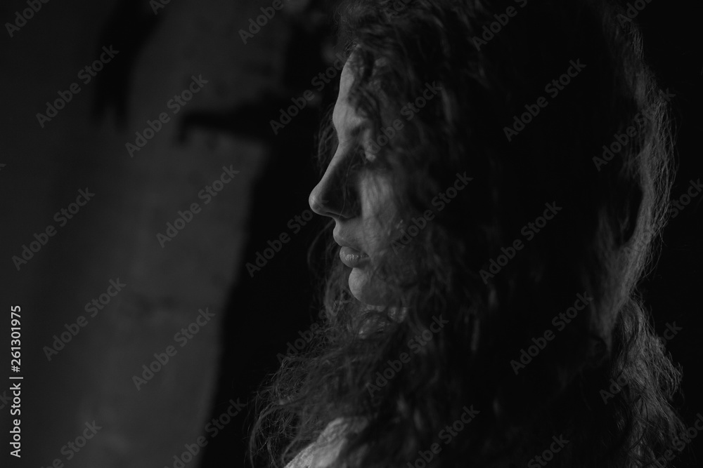 Authentic black and white horizontal portrait of young woman profile, standing in dark room. Close up detailed shot of curly haired sensual Caucasian female, posing indoors. Youth and beauty concept.