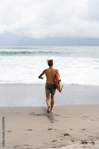 Photography Attractive male surfer in tattoos on the ocean with an orange bright longboard surfboard