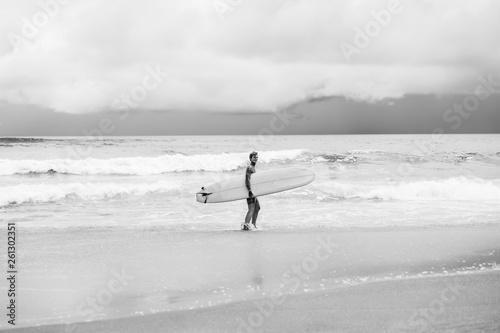 Canvas Print Attractive male surfer in tattoos on the ocean with an orange bright longboard surfboard
