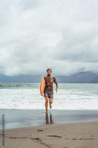 Photography Attractive male surfer in tattoos on the ocean with an orange bright longboard surfboard