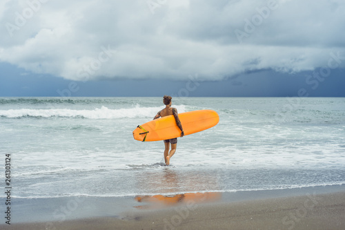 Photography Attractive male surfer in tattoos on the ocean with an orange bright longboard surfboard