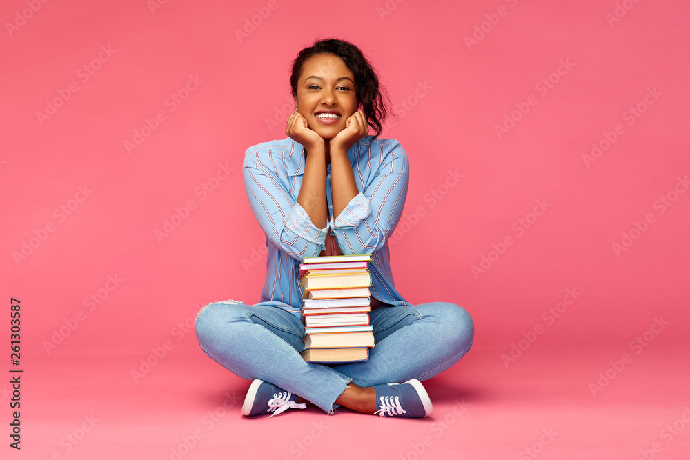 education, high school and people concept - happy african american young student woman with books sitting on floor over pink background education, high school and people concept - happy african american young student woman with books sitting on floor over pink background