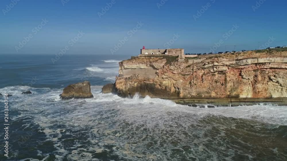 Aerial around view of lighthouse on a cliff with a fortress on the coast of the Atlantic ocean with big waves in Nazare, Portugal, 4k Aerial around view of lighthouse on a cliff with a fortress on the coast of the Atlantic ocean with big waves in Nazare, Portugal, 4k