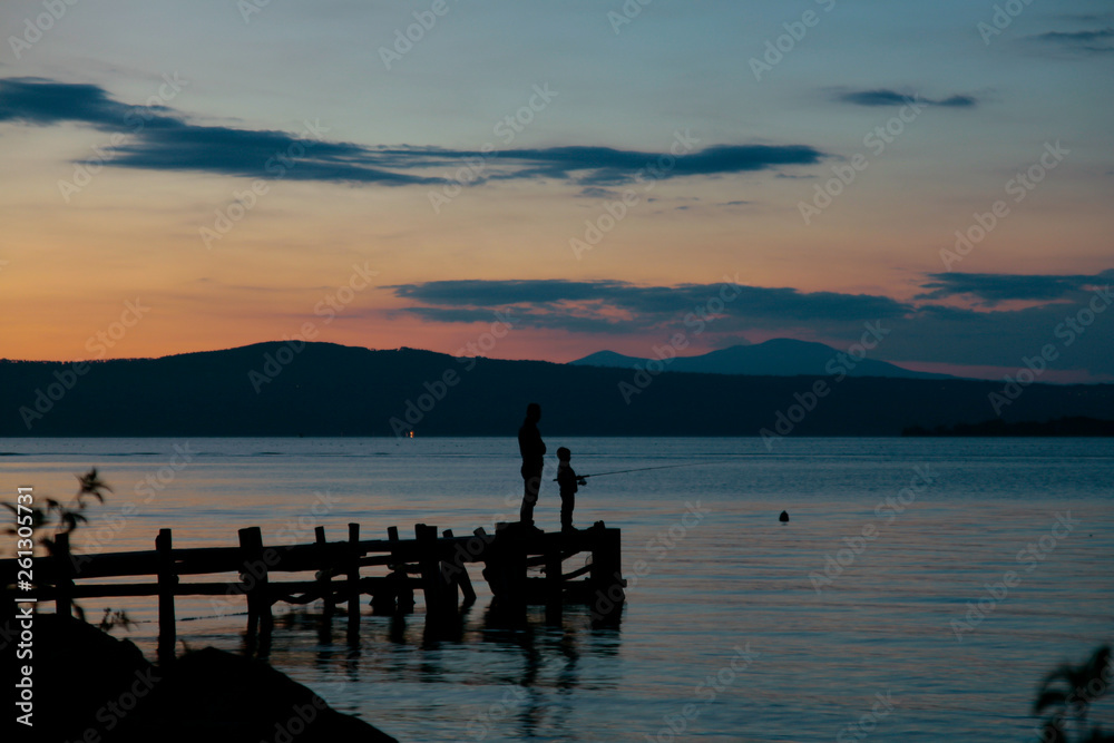 Pesca rilassante su un pontile sul lago calmo al tramonto