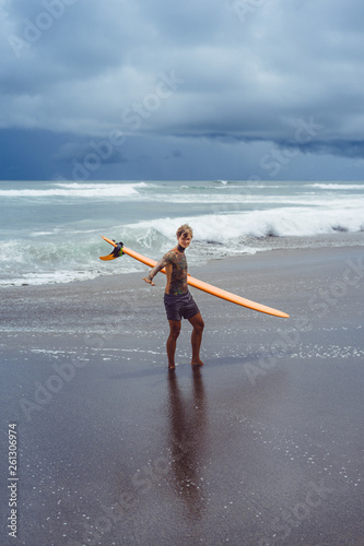 Photography Attractive male surfer in tattoos on the ocean with an orange bright longboard surfboard