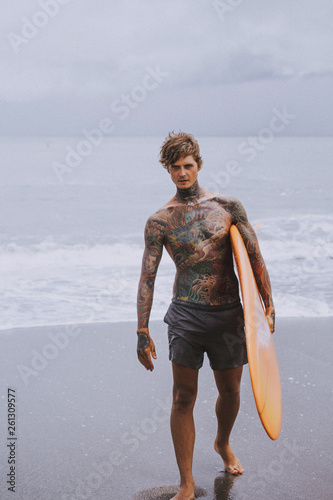 Photography Attractive male surfer in tattoos on the ocean with an orange bright longboard surfboard