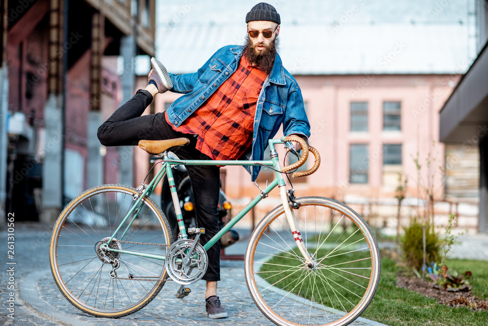 Portrait of a bearded man as a crazy hipster having fun with retro bicycle outdoors on the industrial urban background Portrait of a bearded man as a crazy hipster having fun with retro bicycle outdoors on the industrial urban background