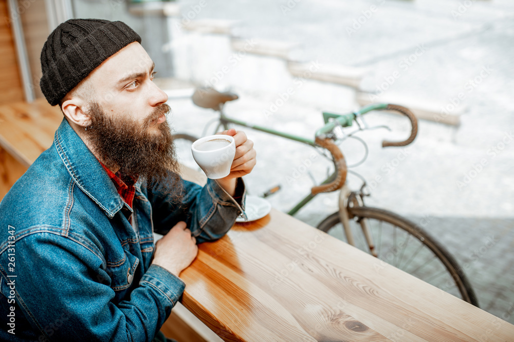 Stylish man enjoying a coffee drink while sitting at the cafe near the window with retro bicycle outdoors
