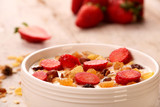 Bowl of yogurt with strawberries and granola muesli, over a white wood background.