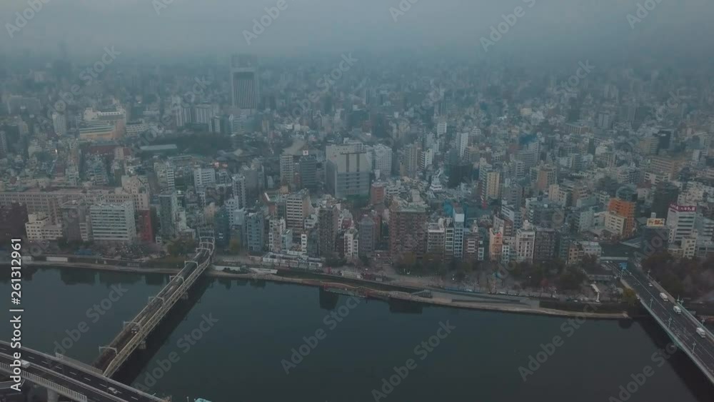 Aerial drone slowly panning towards a bustling highway bridge full of traffic next to a canal and a skyline of high rise buildings on an overcast grey day with polluted smog filled skies Aerial drone slowly panning towards a bustling highway bridge full of traffic next to a canal and a skyline of high rise buildings on an overcast grey day with polluted smog filled skies