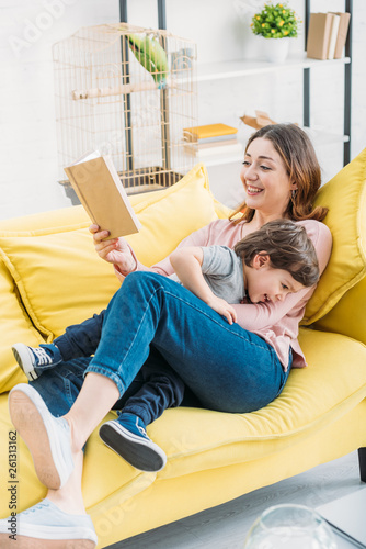 smiling mother with book having fun with adorable son on sofa at home