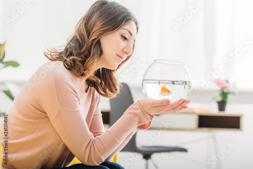 beautiful smiling woman holding aquarium with gold fish at home