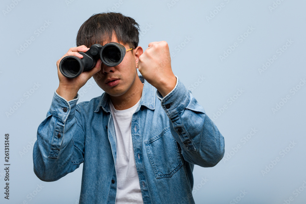 Young chinese man holding a binoculars showing fist to front, angry expression Young chinese man holding a binoculars showing fist to front, angry expression