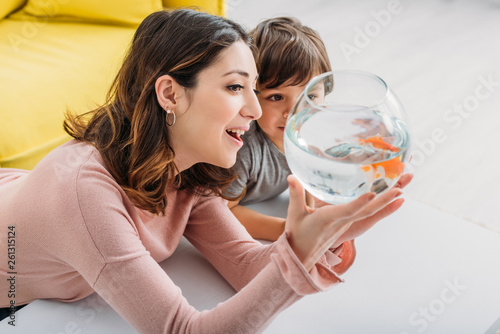 Schilderij op canvas smiling attractive woman showing fish bowl to adorable son