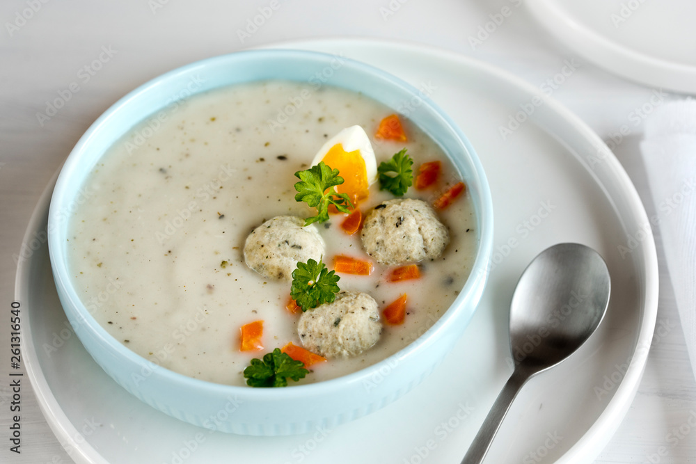 A plate with white Polish soup. White borsch with egg, meatballs, cottage cheese and carrots. A plate with white Polish soup. White borsch with egg, meatballs, cottage cheese and carrots.